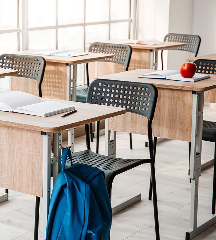 A classroom with tables and chairs and a backpack hanging from a chair.