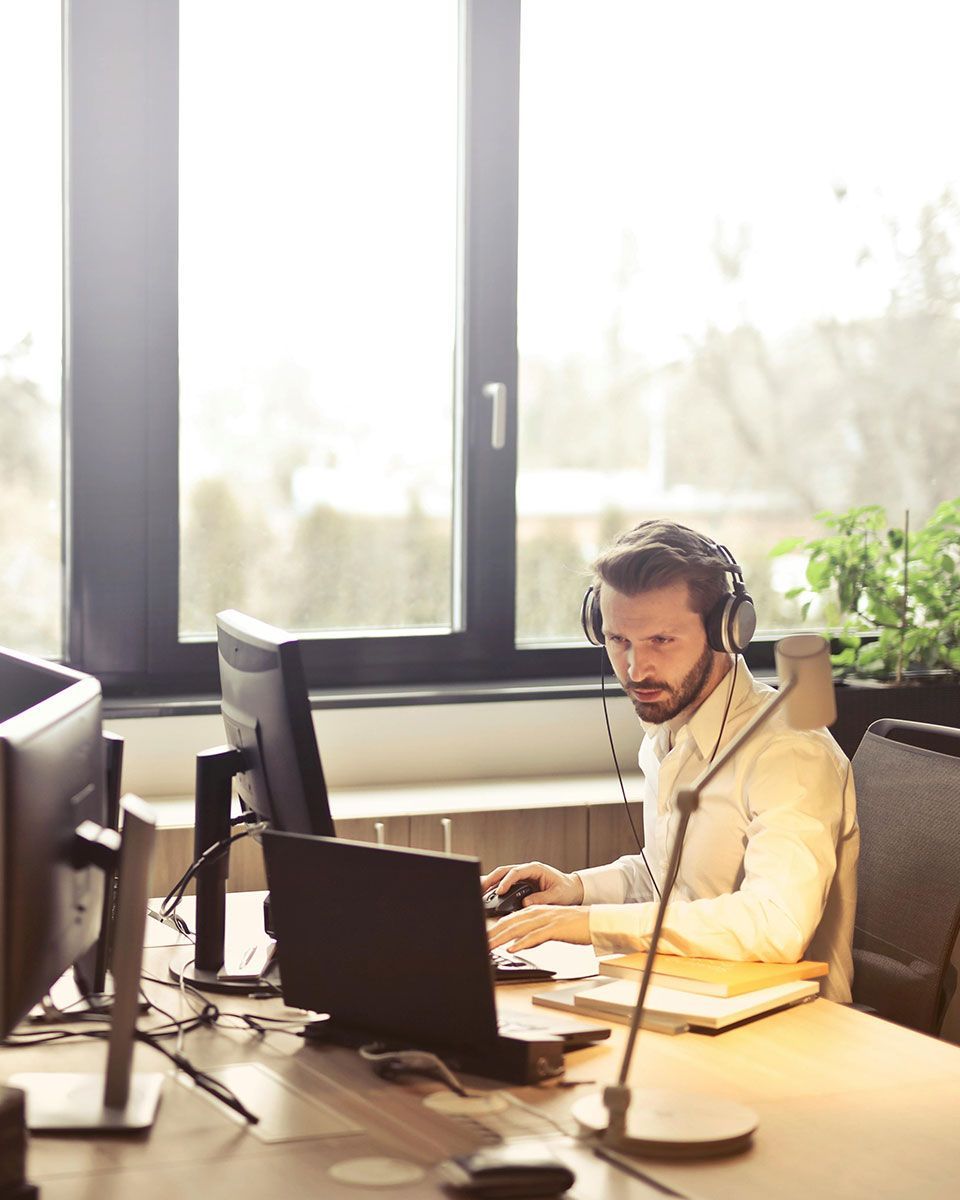 A man wearing headphones is sitting at a desk in front of a computer.
