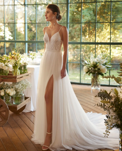Blonde bride in a white strapless gown with tulle cape, outdoors in front of a building with a palm tree.