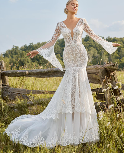 Woman in a wedding dress stands beside a lion statue, in front of a mansion.