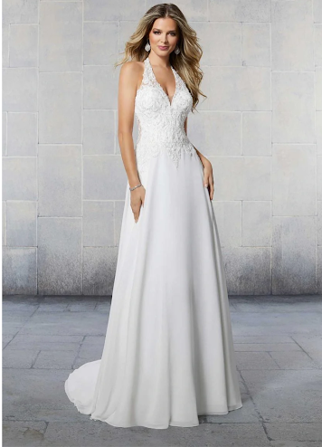 Woman in a white, off-shoulder mermaid wedding dress with a long train, standing in a white studio.