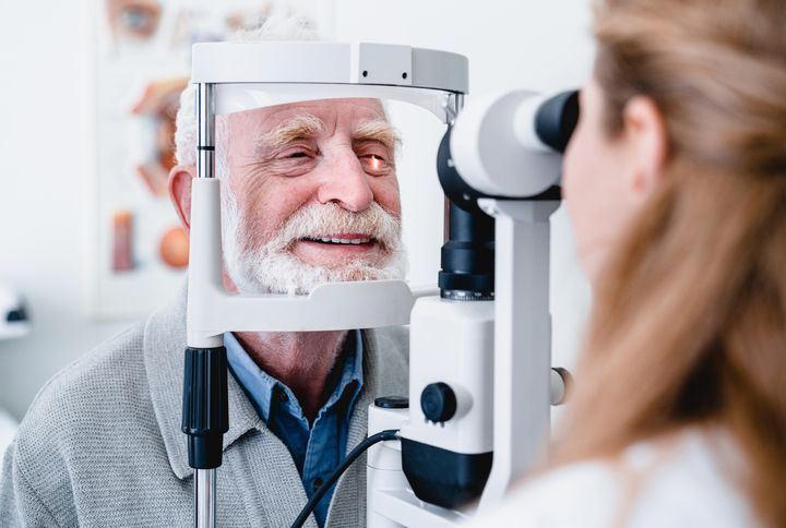 Smiling cheerful elderly patient being checked on eye by female ophthalmic doctor