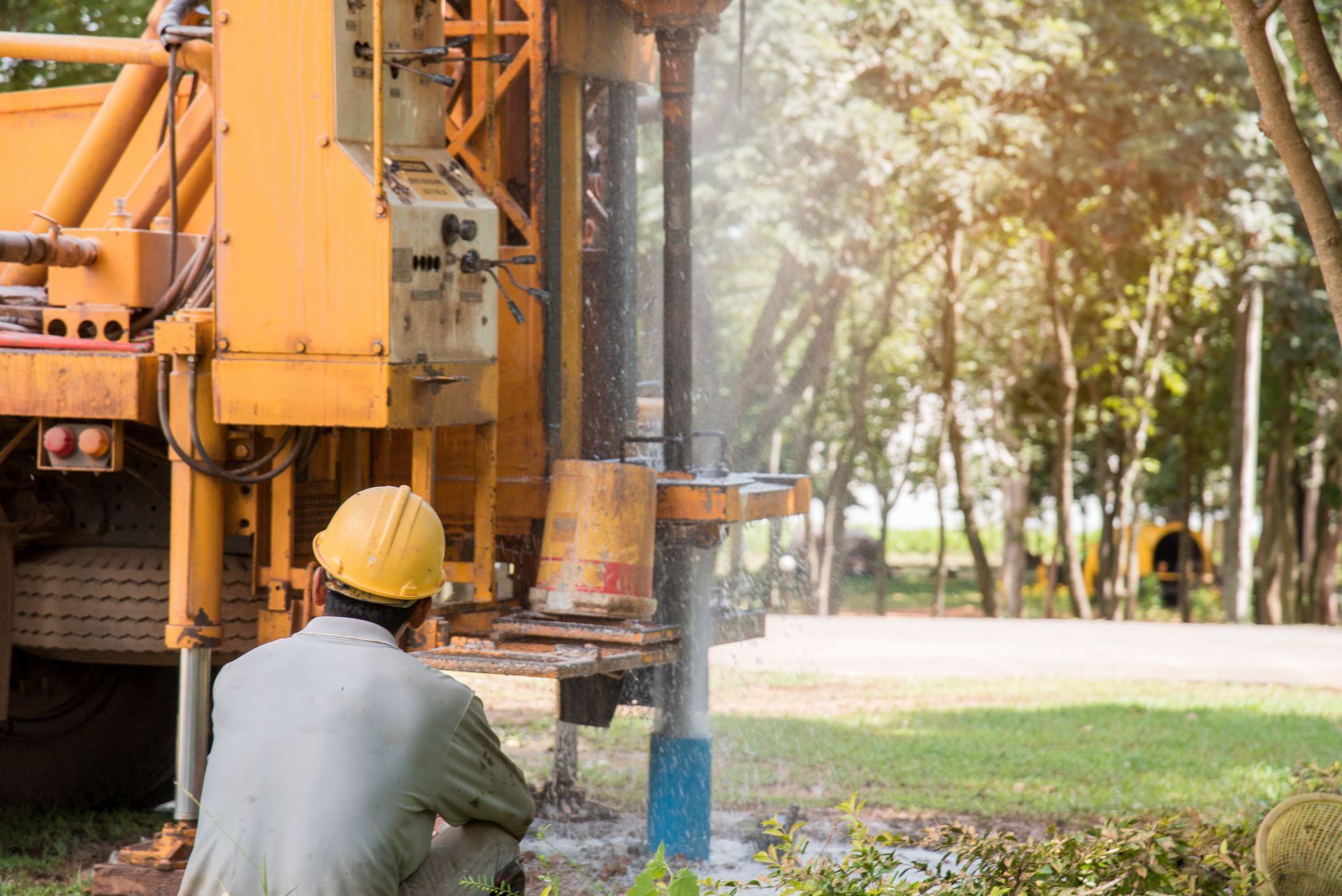 A technician monitors a rig during a commercial water well drilling project on a grassy landscape.