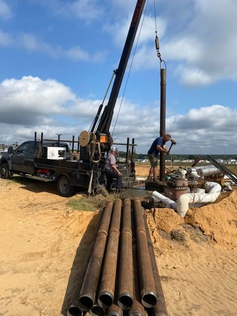 Person in orange work clothes working on a concrete manhole, using their gloved hands.