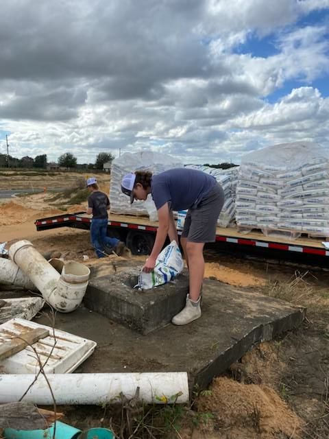 Black water tank and white pressure tank with pump system on a concrete pad outdoors.