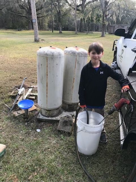 Stone well in a grassy field, surrounded by trees and a gravel border.