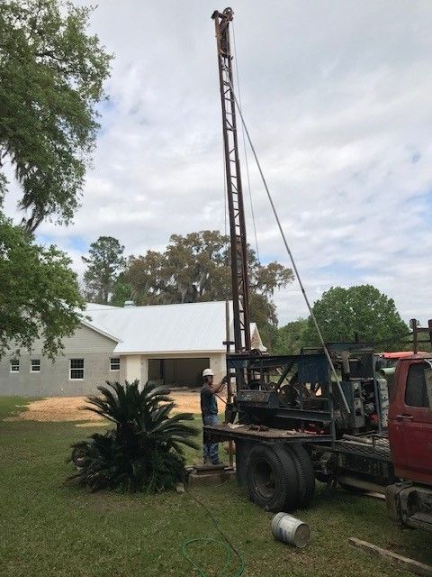 Person operating a drilling machine, creating a well. Outdoors, sunny day.