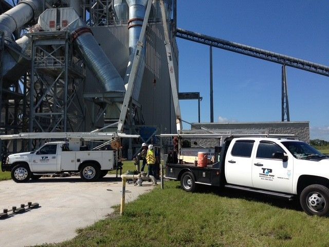 Plumber connecting PVC pipe fittings outdoors near a well, wearing gloves, with blue and white pipes.