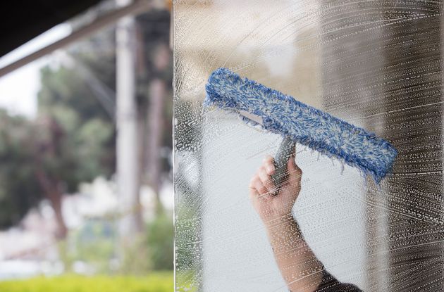 A person using a blue microfiber window washer tool to clean a glass surface covered in soapy water.