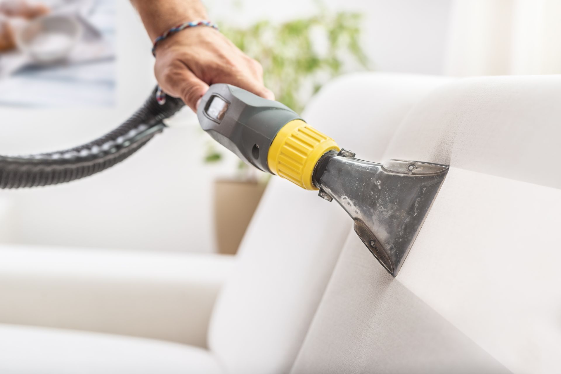 A person uses a handheld steam cleaner nozzle to clean a white upholstered sofa.