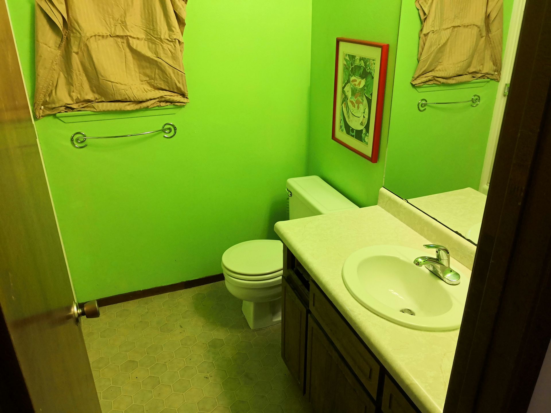 A small bathroom with lime green walls, a white toilet, a wood-toned vanity, and a framed artwork on the wall.