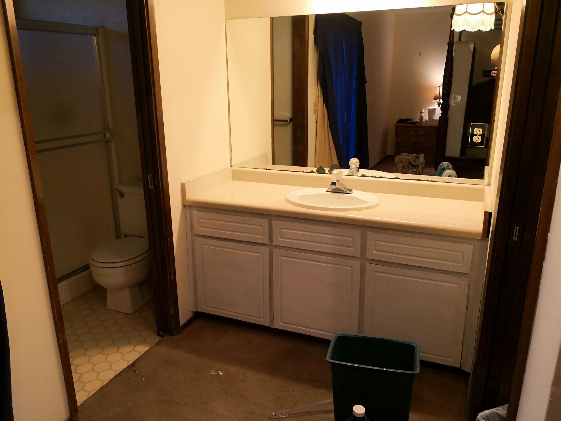 A bathroom with a white vanity, a large mirror, a sink, and a toilet in a separate alcove with a dark floor.