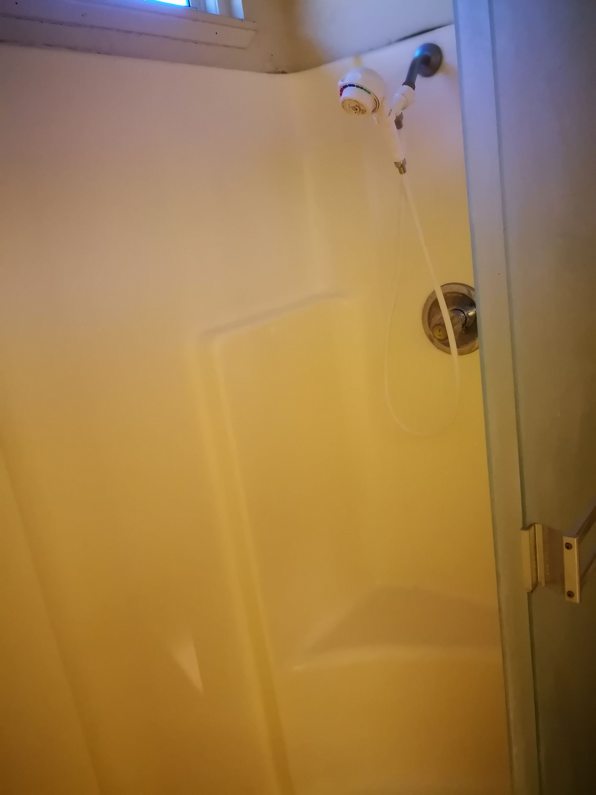 A white fiberglass shower stall featuring a mounted shower head and a built-in seat against the back wall.