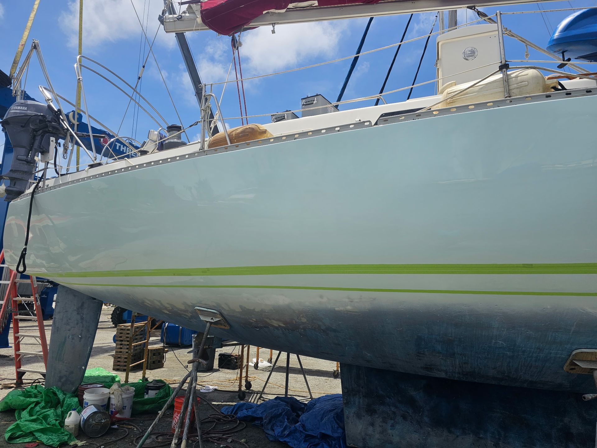 A white sailboat with a green stripe on the side is sitting on the ground.