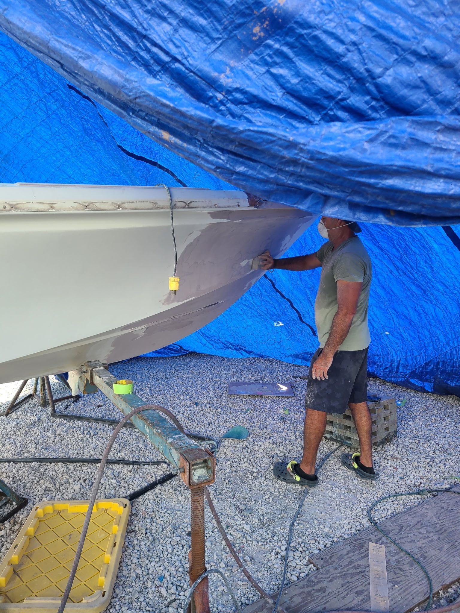 A man is painting a boat under a blue tarp.