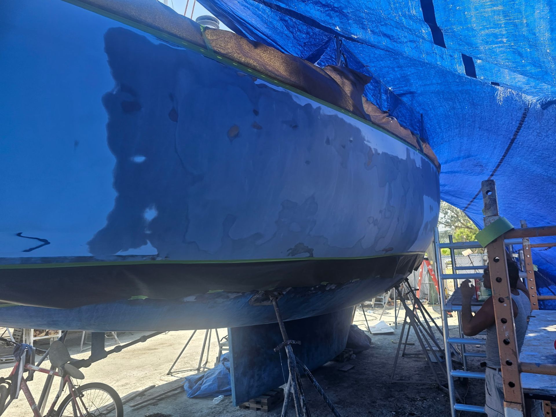 A man is painting a boat with a blue tarp.
