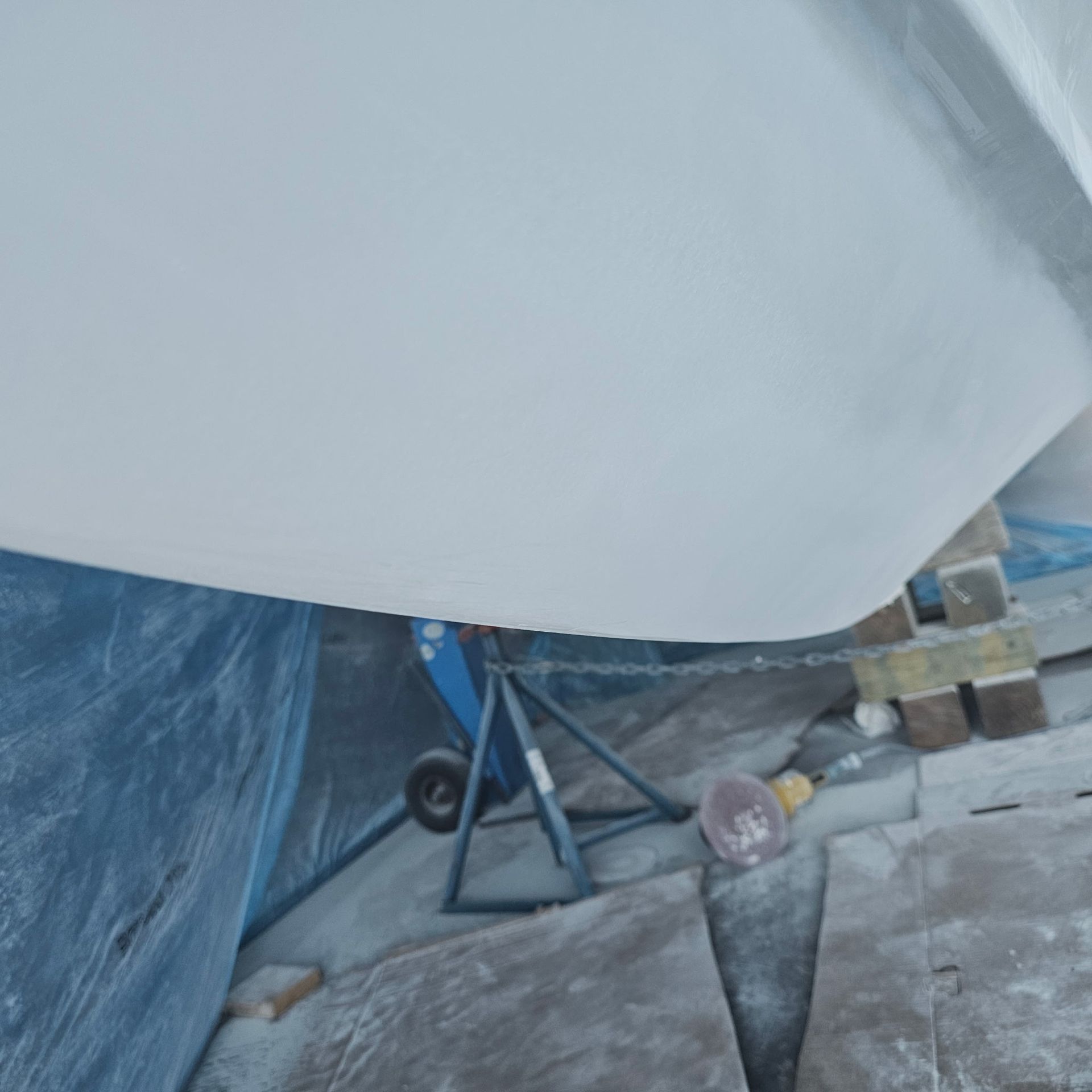 A white boat is sitting on a blue tarp on the ground