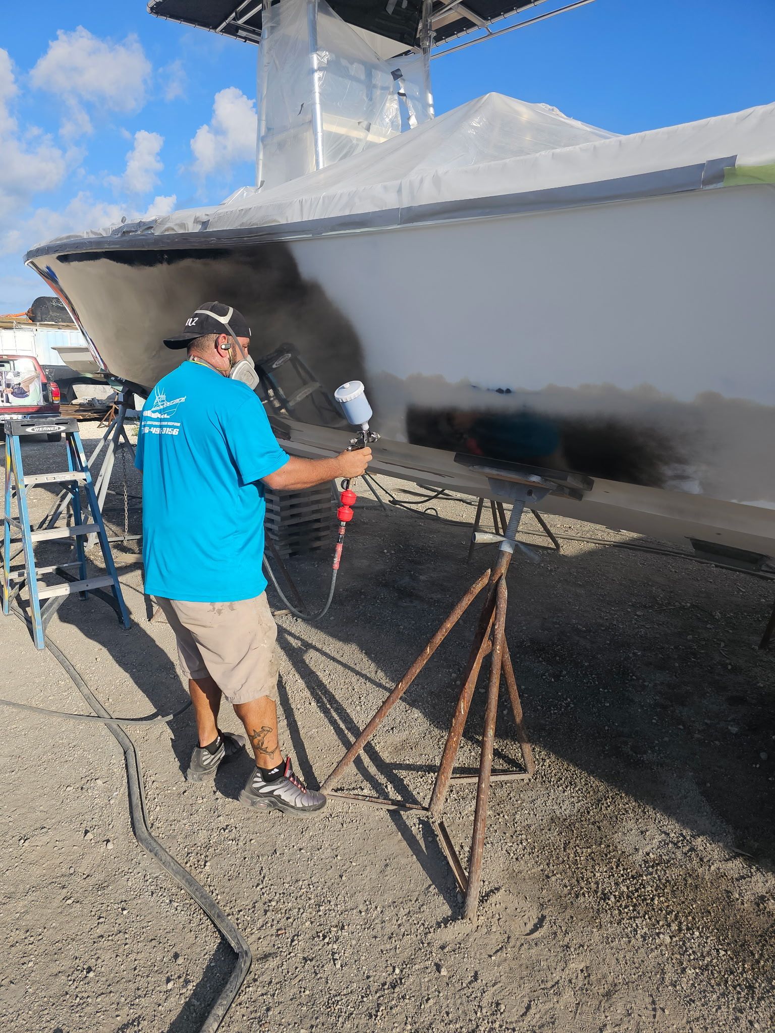 A man in a blue shirt is spray painting a boat.