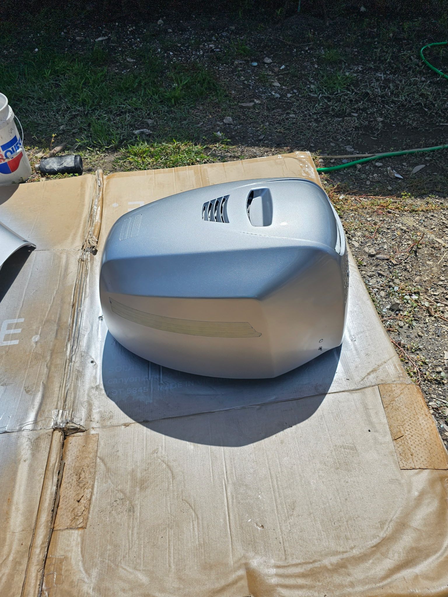 A silver side mirror is sitting on top of a piece of cardboard.