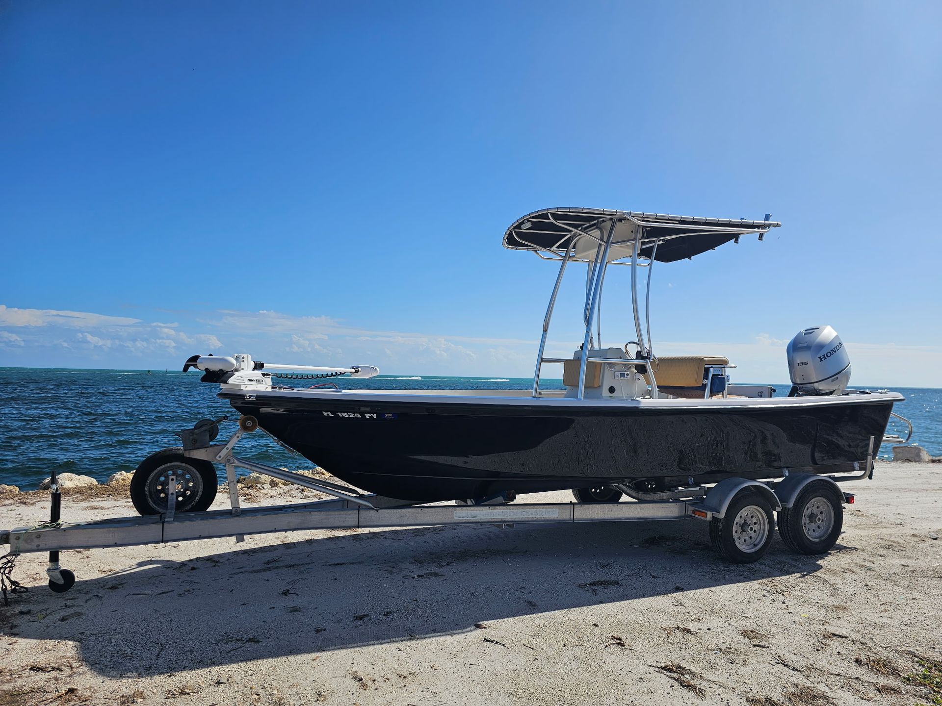 A boat on a trailer is parked on the beach near the ocean.