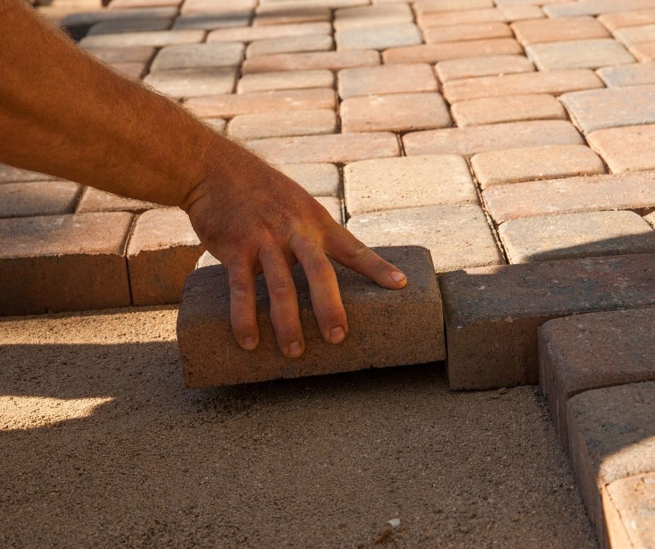 A person is laying bricks on a concrete surface.