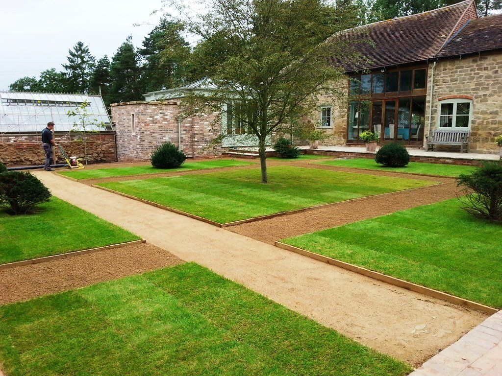 A man is mowing a lush green lawn in front of a stone building.