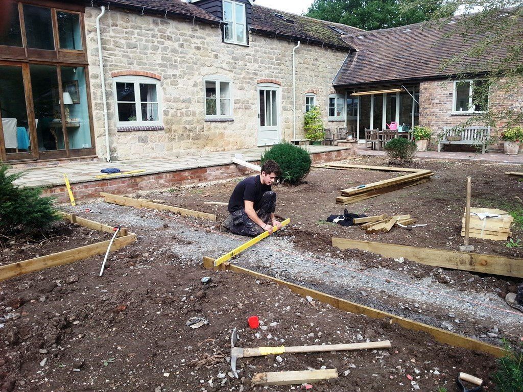 A man is kneeling down in the dirt in front of a house.