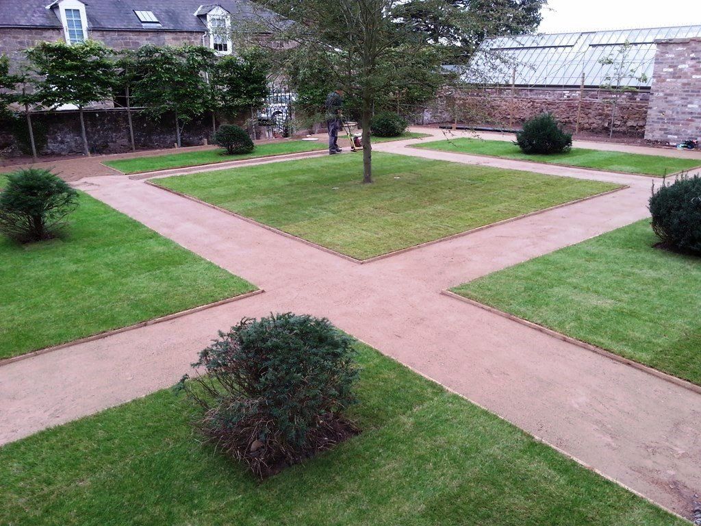 A lush green garden with a brick walkway and trees.