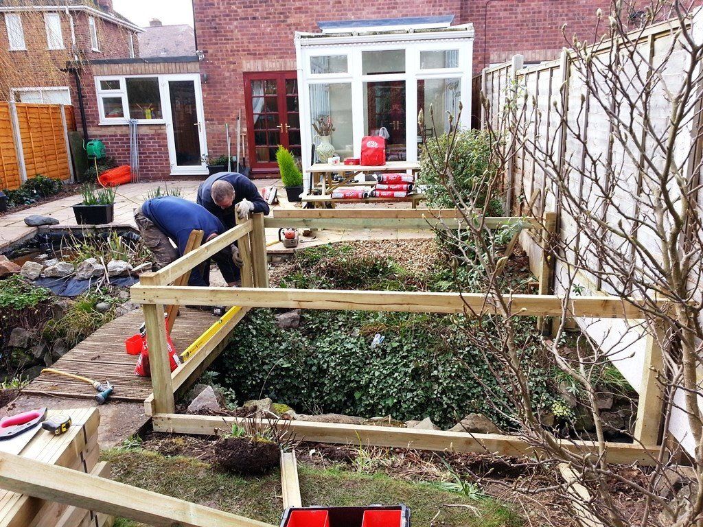Two men are working on a wooden fence in a garden.