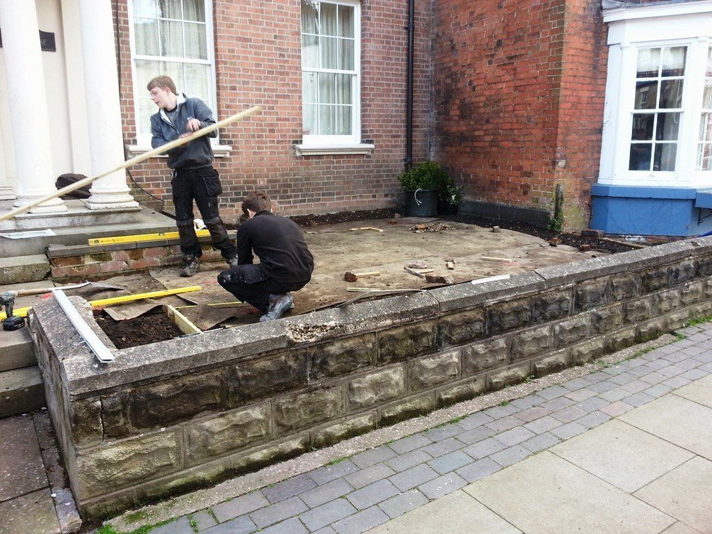 Two men are working on the sidewalk in front of a brick building.