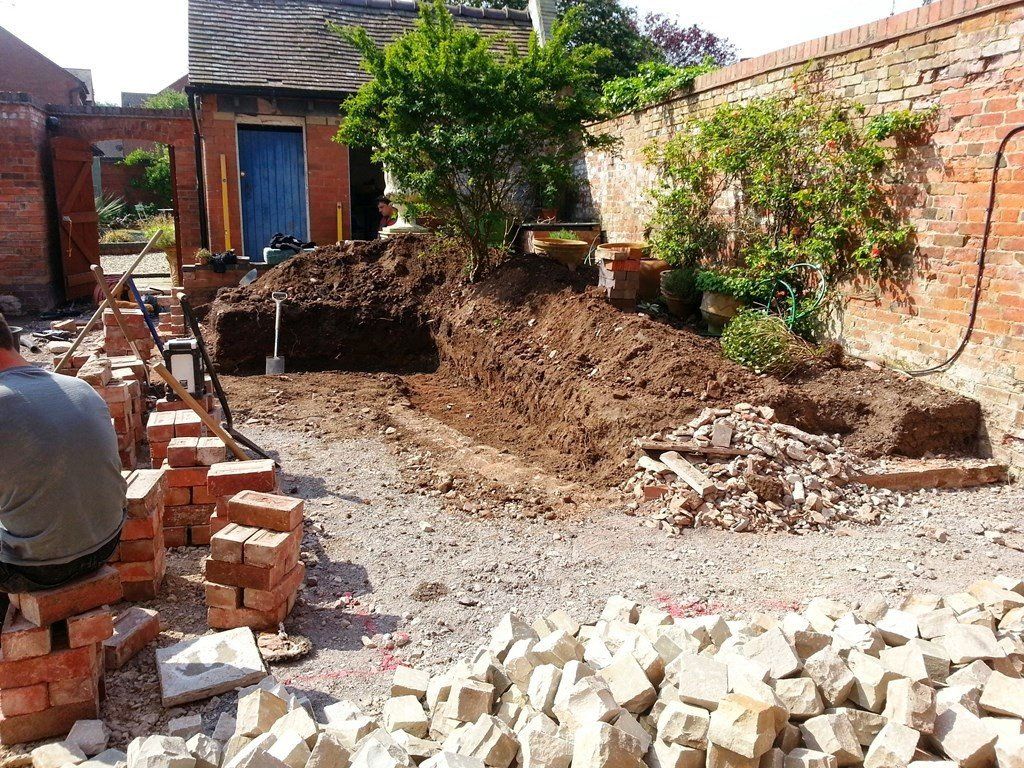 A man is sitting on a pile of bricks in a yard.
