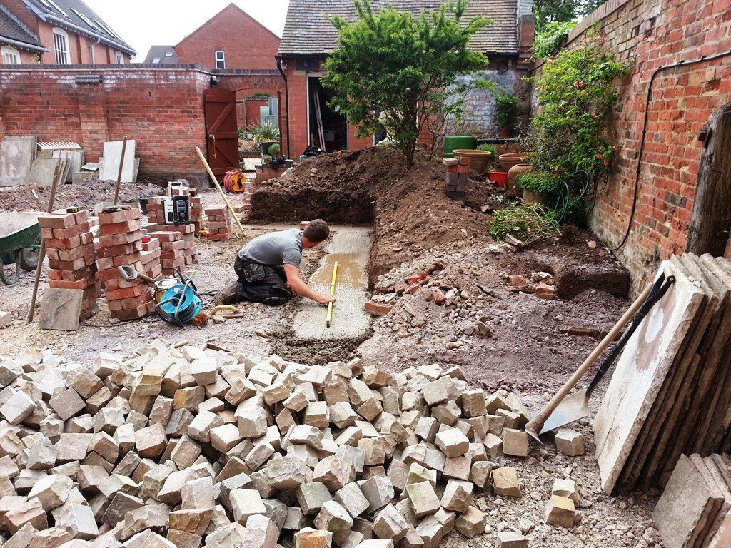 A man is kneeling down in a pile of bricks in a yard.