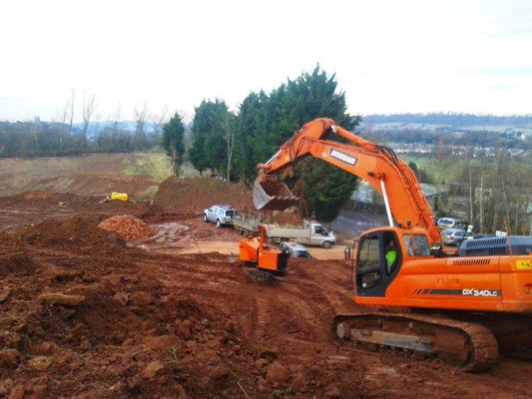 A large orange excavator is moving dirt on a construction site.