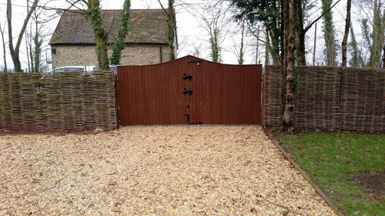 There is a wooden gate in the middle of a gravel driveway.