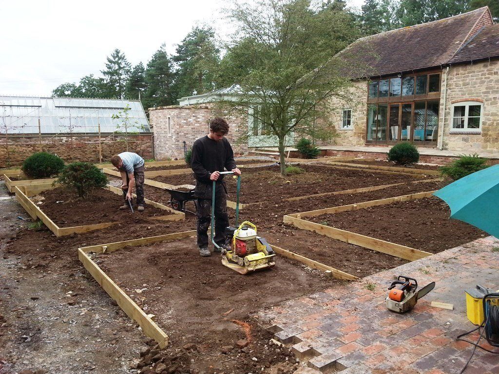 A man is using a machine to level the ground in a garden.