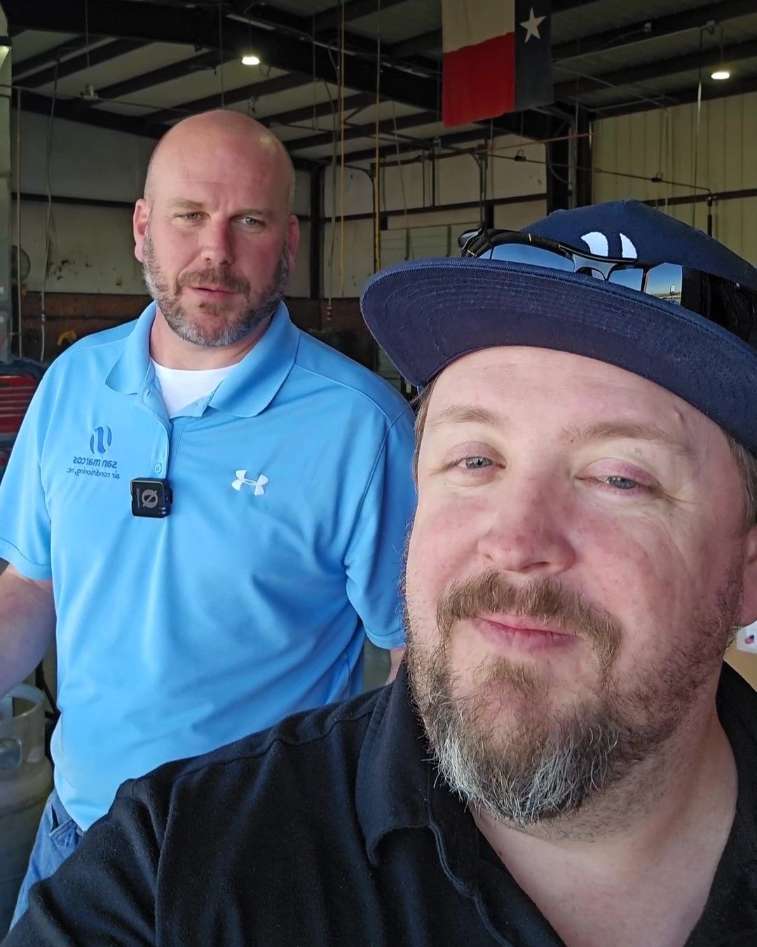 A man wearing a blue under armour shirt stands next to another man wearing a hat