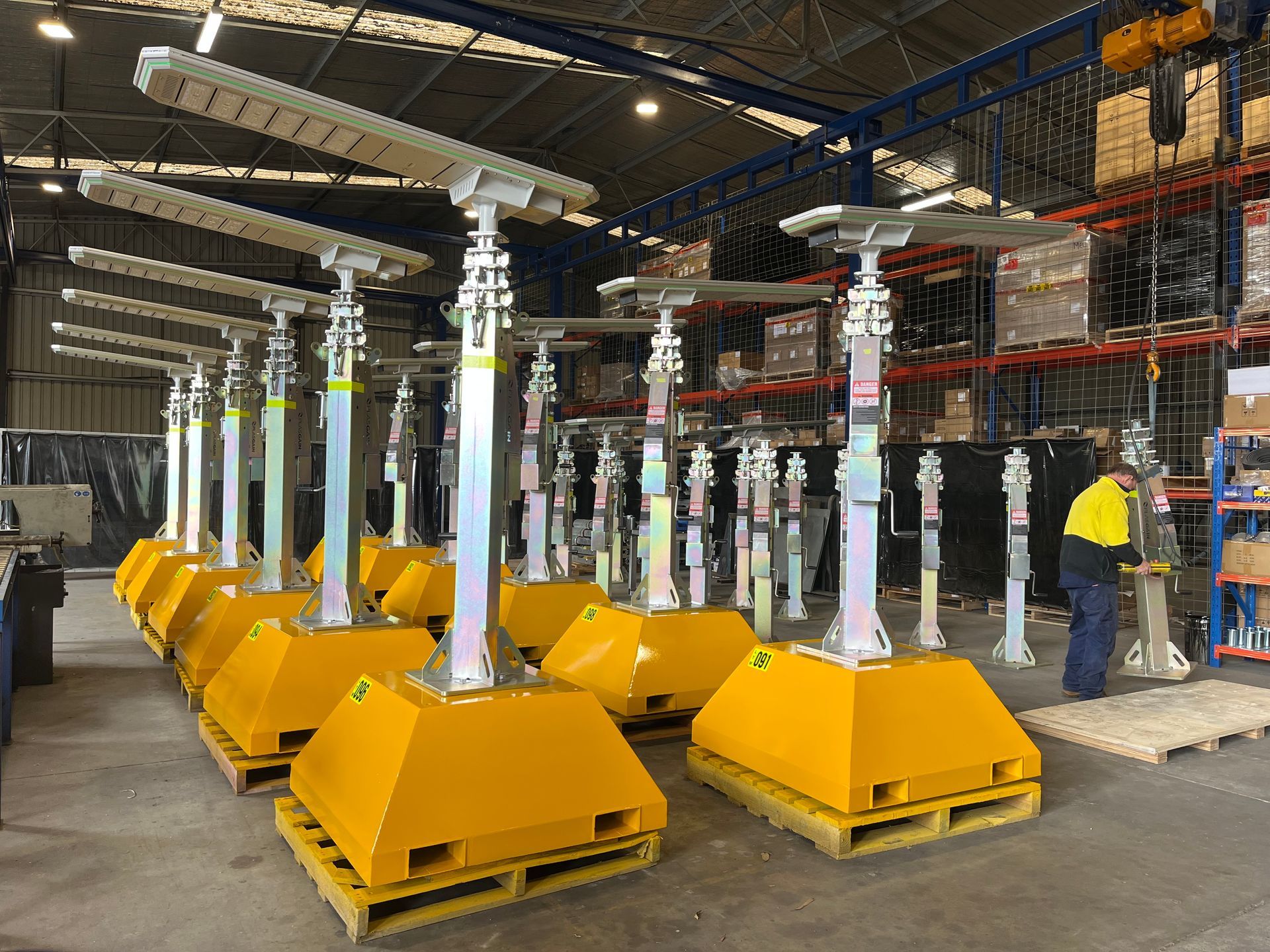 Yellow industrial jack stands on pallets in a warehouse, with a worker standing in the background.