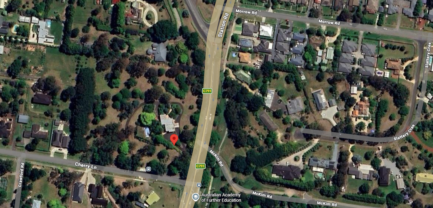 A satellite view of a suburban area bisected by a highway, with a red map pin marking a property in a wooded lot.