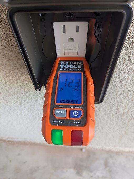 Orange electrical outlet tester plugged into outdoor outlet, displaying 