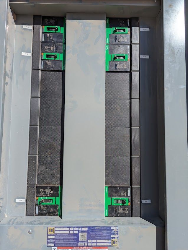 Electrical panel with circuit breakers, various sizes, mounted in a metal enclosure.