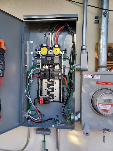 Open electrical panel on an outdoor wall. Wires, breakers, and meters are visible.