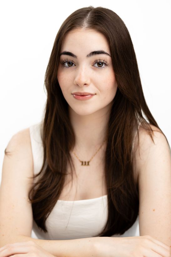 A woman is sitting at a desk with a laptop and a vase of flowers.