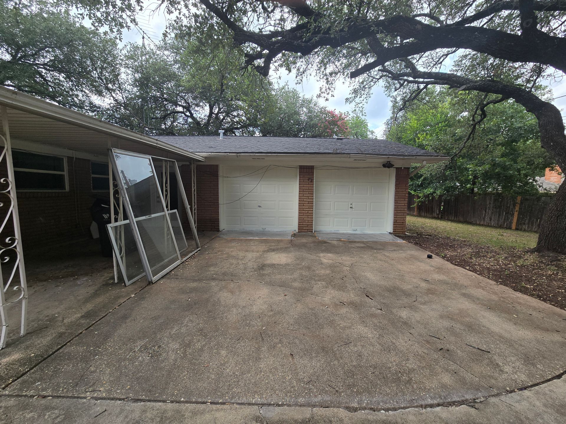 Concrete driveway leading to a garage and house with several window frames leaning against the side.