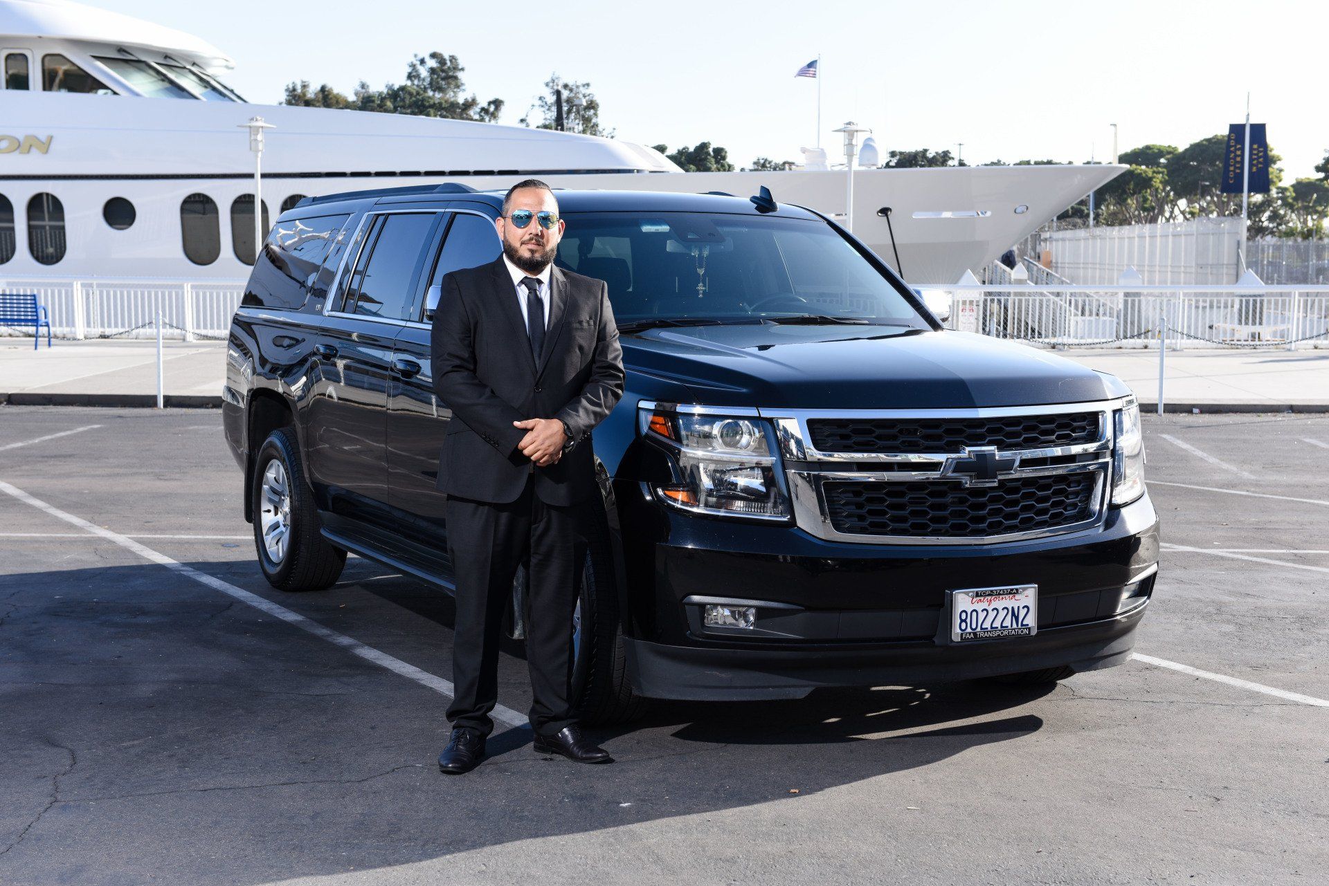 a man in a suit and tie is standing next to a black suv in a parking lot .