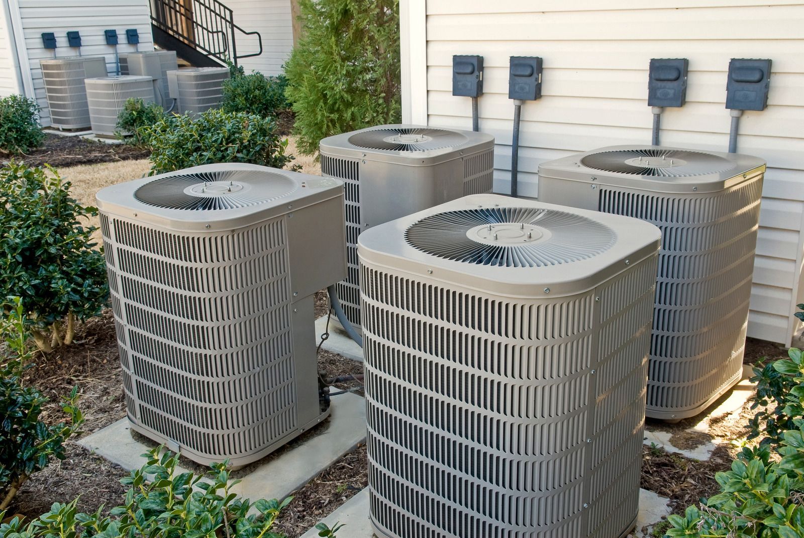 A bunch of air conditioners are sitting outside of a house.