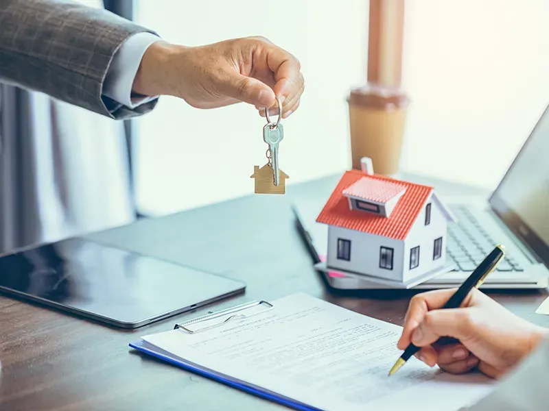 Un hombre le da una llave a una mujer que está firmando un contrato.