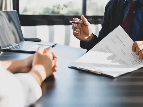 Un hombre y una mujer están sentados en una mesa con papeles y una computadora portátil.