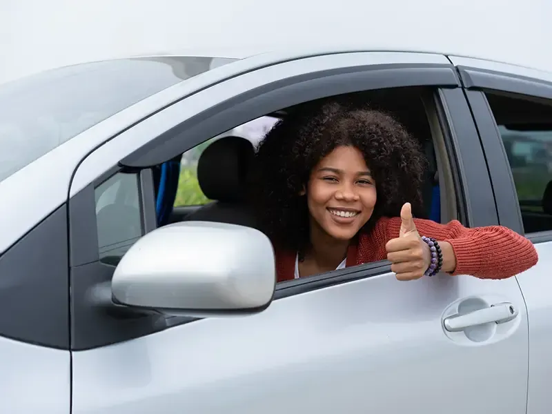 Una mujer hace un gesto de aprobación con el pulgar mientras está sentada en un automóvil.