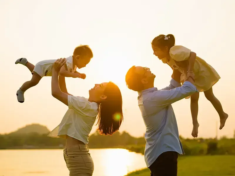 Una familia está jugando con sus hijos cerca de un lago al atardecer.