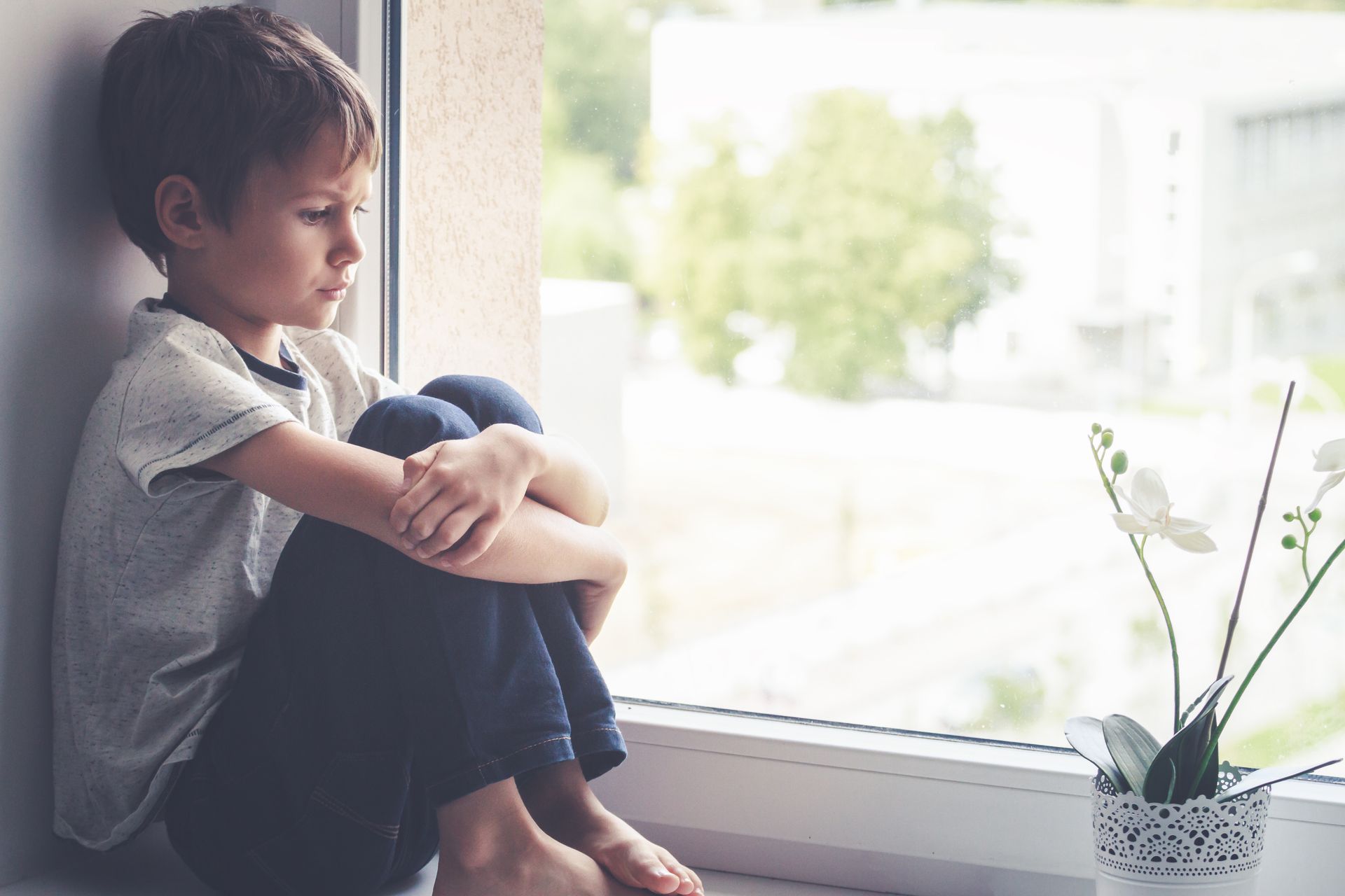 sad young boy looking out of the window at home
